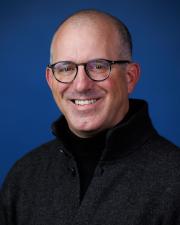 Smiling man with dark rimmed glasses and dark shirt and sweater