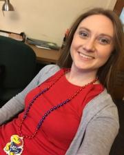 Smiling young woman on a desk chair in a red shirt and grey sweater